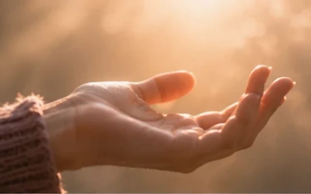 Mão se abrindo lentamente de um punho fechado em direção à luz quente — o alívio de soltar o ritual