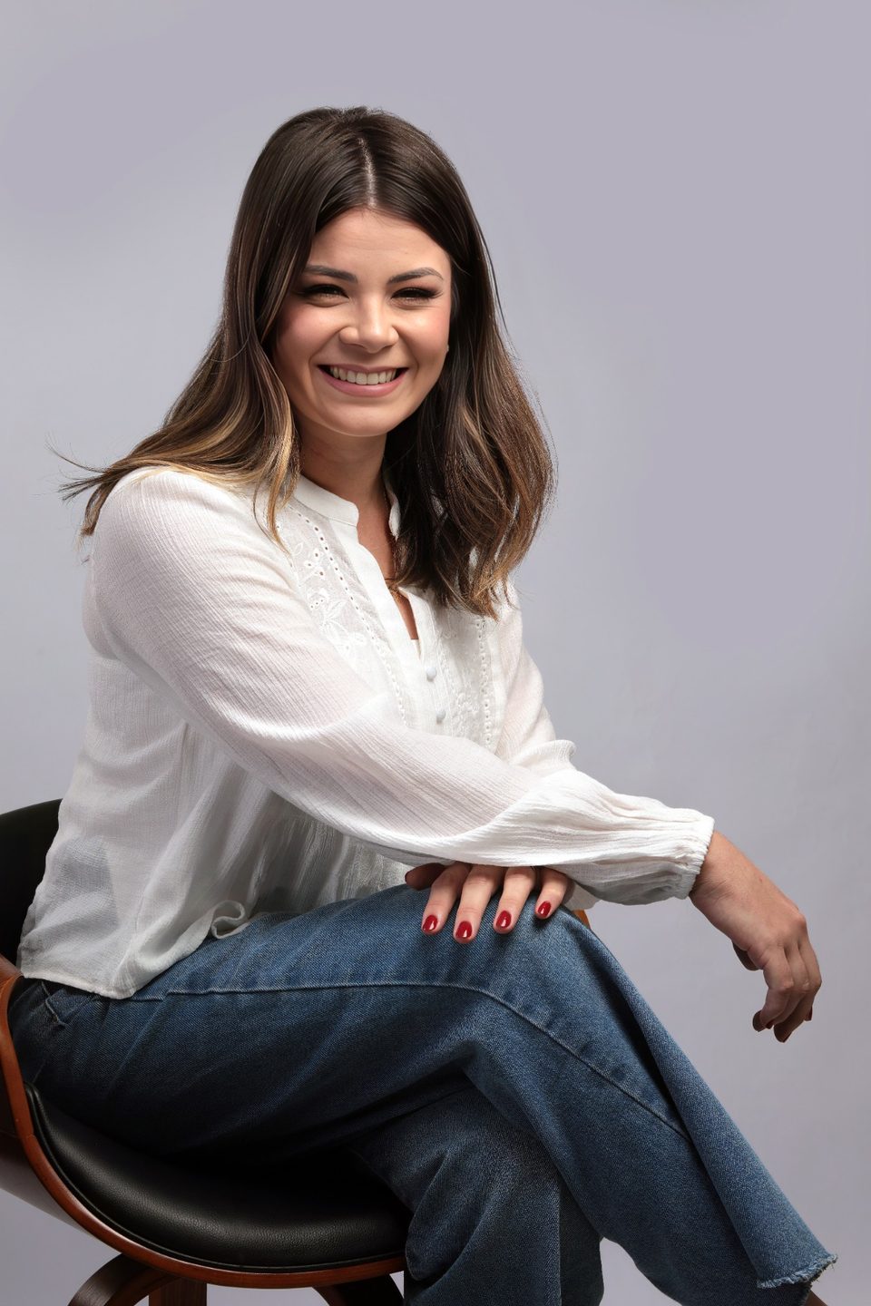 Samara sentada de lado, sorrindo, num banquinho de madeira