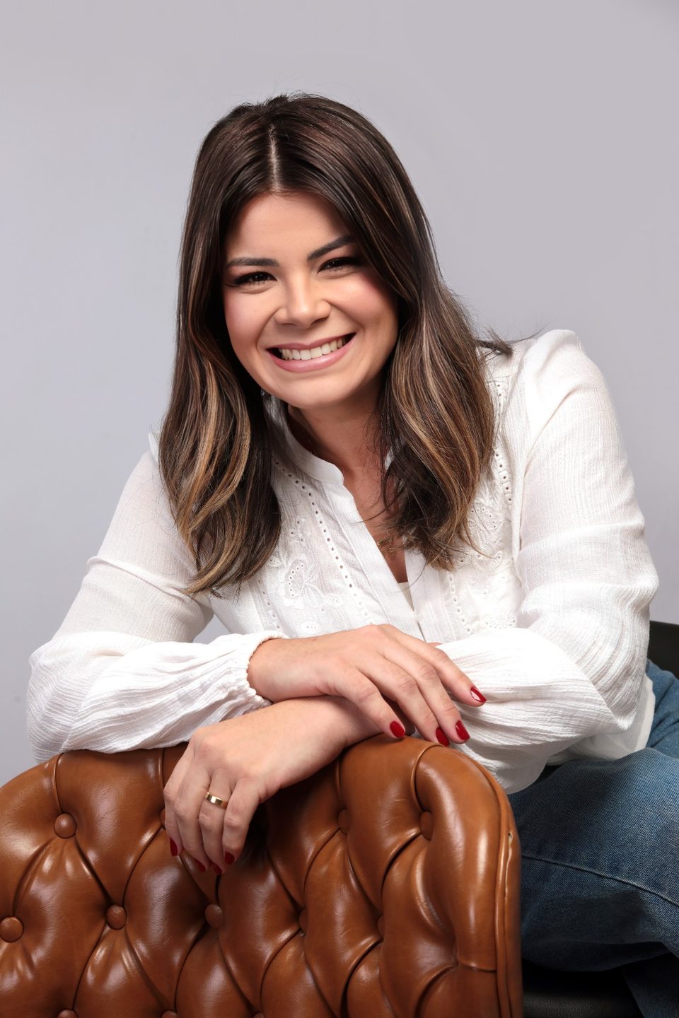Samara Gregório sorrindo, apoiada num sofá de couro caramelo